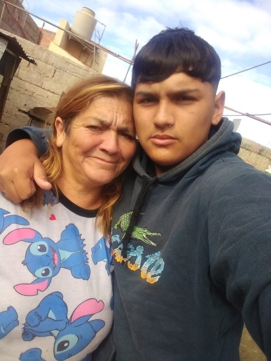 Mujer en uniforme de limpieza frente a una escuela en Comodoro Rivadavia