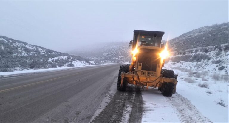 Ruta nevada en Chubut con señal de tránsito y montañas de fondo