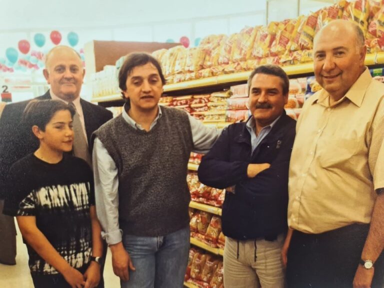 Carlos Linares joven junto a un grupo de personas en el interior de un local con góndolas cargadas de productos y globos de colores