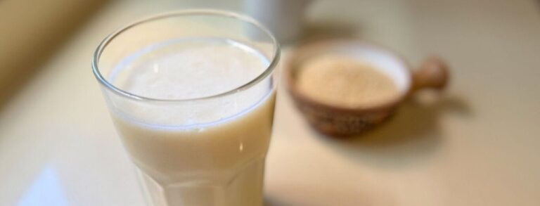 Vaso con leche de quinoa casera junto a quinoa en granos y una botella de vidrio